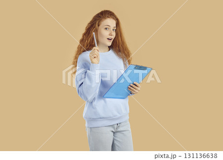 Smiling teenage girl with clipboard and pen comes up with an idea for her project. 131136638