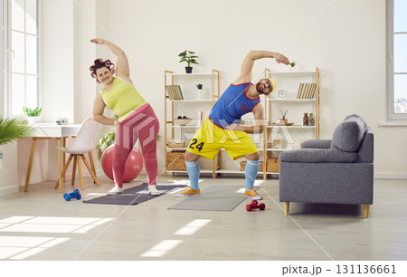 Fat woman with funny bearded man in bright sportswear doing sport exercises at home together. 131136661