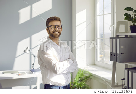 Businessman in white shirt standing in the office with crossed arms looking at camera and smiling. 131136672
