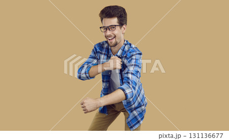 Happy male student in a plaid shirt and glasses dancing on a beige color background Happy male student in a plaid shirt and glasses dancing on a beige color background 131136677