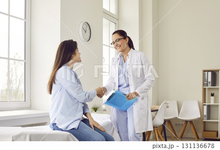 Friendly doctor shaking hands with a young patient woman in medical clinic after exam. Friendly doctor shaking hands with a young patient woman in medical clinic after exam. 131136678
