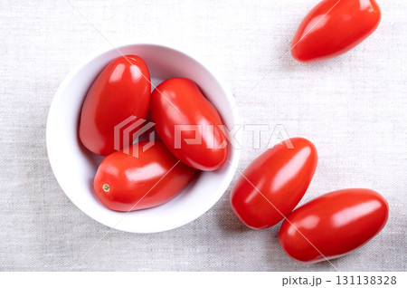 Fresh plum tomatoes, Roma tomatoes in a white bowl, on linen. Also known as processing or paste tomatoes, oval shaped, used for canning or producing tomato paste, because of its slender, firm nature. Fresh plum tomatoes, Roma tomatoes in a white bowl, on linen. Also known as processing or paste tomatoes, oval shaped, used for canning or producing tomato paste, because of its slender, firm nature. 131138328