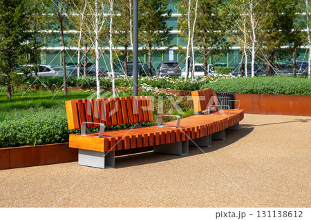 Contemporary wooden bench in landscaped park area with green grass and seasonal flowers. comfortable urban environment. improvement, beautification, renovation of urban environment 131138612