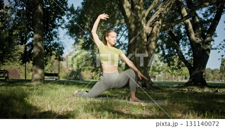 young beautiful white girl doing yoga in park among trees in clearing on summer day 131140072