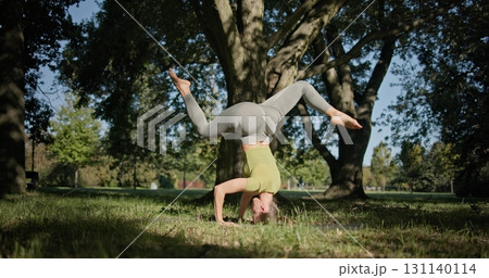 young beautiful white girl doing yoga in park among trees in clearing on summer day 131140114