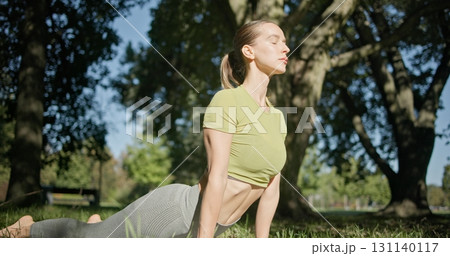 young beautiful white girl doing yoga in park among trees in clearing on summer day 131140117