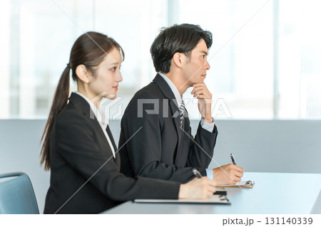 デスクに座り書類に記入しながら話を聞くスーツ姿のビジネスマンとビジネスウーマン 131140339