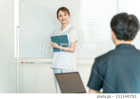 医療カンファレンスなどでホワイトボードの前で説明する看護師,薬剤師,管理栄養士の女性スタッフ 131140783
