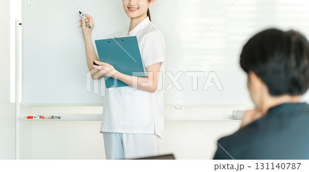 医療カンファレンスなどでホワイトボードの前で説明する看護師,薬剤師,管理栄養士の女性スタッフ 131140787