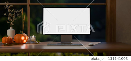 White screen computer and jack-o-lantern halloween pumpkins and candles on wooden table aside window White screen computer and jack-o-lantern halloween pumpkins and candles on wooden table aside window 131141008