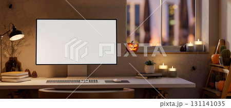 White screen computer on table with halloween pumpkin lanterns and candles on window in dim lit room 131141035