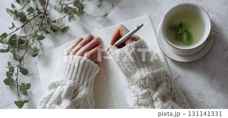 An overhead shot of a woman writing in a journal with a cup of mint tea. 131141331