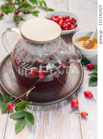 Steaming rosehip tea brewing in glass teapot with honey and fresh rose hips 131142025