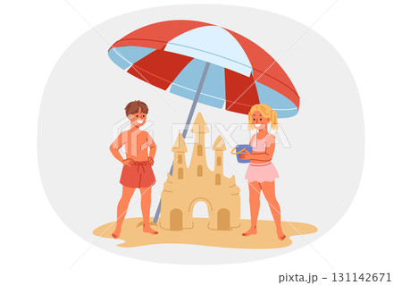 Children build sand castle on beach, standing with umbrella to protect them from sun Children build sand castle on beach, standing with umbrella to protect them from sun 131142671