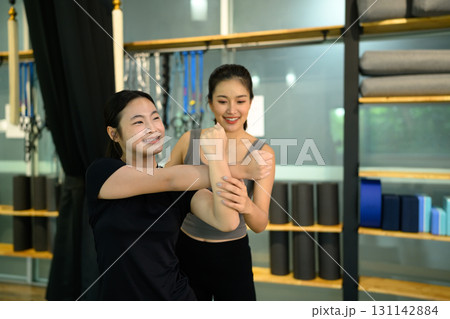 Female trainer guiding teenage girl through an arm stretch exercise in a fitness studio Female trainer guiding teenage girl through an arm stretch exercise in a fitness studio 131142884