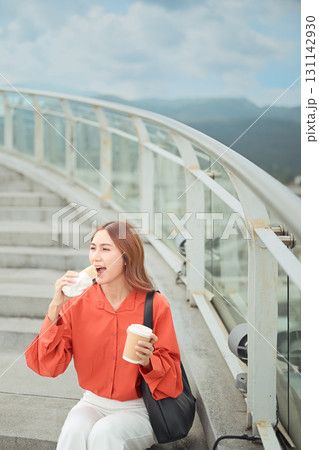 Relaxed businesswoman having morning meal on staircase with coffee cup in hand 131142930