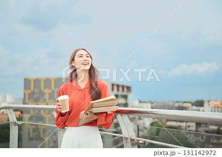 Happy businesswoman enjoying coffee break while standing on rooftop with city skyline Happy businesswoman enjoying coffee break while standing on rooftop with city skyline 131142972