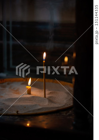 Lit church candles in sand tray, symbolic prayer and remembrance in dim sacred space Lit church candles in sand tray, symbolic prayer and remembrance in dim sacred space 131144335