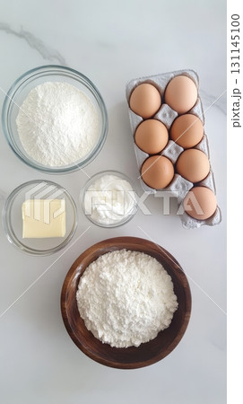 Raw ingredients for scone preparation are neatly arranged on a kitchen countertop, showcasing flour, eggs, butter, and cream 131145100