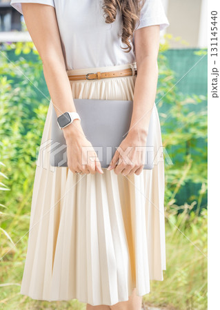 Woman in elegant pleated skirt holding a laptop outdoors. Concept of modern femininity, mobile work and stylish tech-savvy lifestyle. Woman in elegant pleated skirt holding a laptop outdoors. Concept of modern femininity, mobile work and stylish tech-savvy lifestyle. 131145440
