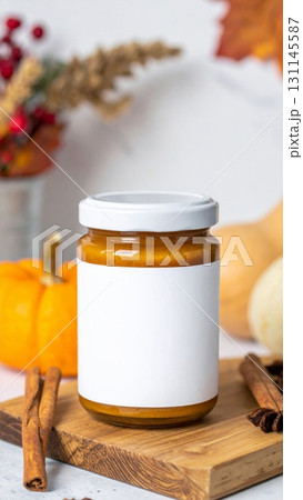 Pumpkin Jam in Clear Jar with White Lid Surrounded by Cinnamon Sticks and Pumpkins 131145587