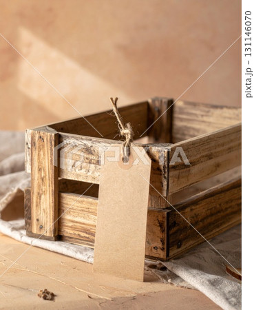 Brown Wooden Crate with Blank Tag on Burlap Surface with Neutral Background 131146070