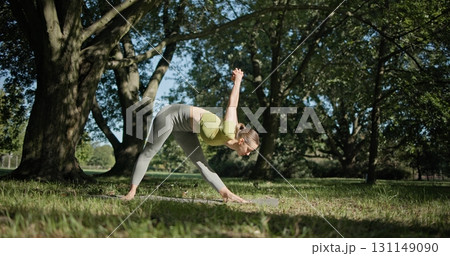young beautiful white girl doing yoga in park among trees in clearing on summer day 131149090