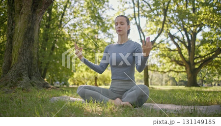 A young beautiful white girl practices yoga in the park and meditates in the lotus position among the trees in a clearing on a summer day A young beautiful white girl practices yoga in the park and meditates in the lotus position among the trees in a clearing on a summer day 131149185