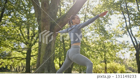 young beautiful white girl doing yoga in park among trees in clearing on summer day 131149233