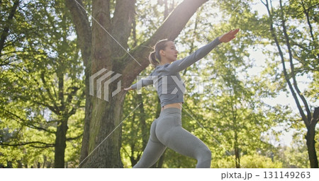 young beautiful white girl doing yoga in park among trees in clearing on summer day 131149263