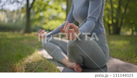 A young beautiful white girl practices yoga in the park and meditates in the lotus position among the trees in a clearing on a summer day 131149325