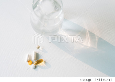 Ice water glass and assorted vitamins with long morning shadows on a light surface 131150241