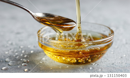 Honey or aroma oil or liquid olive oil falls pours into a clear glass bowl. Clear gel serum texture. Cosmetic gel skincare cream product close up The concept of skin care or eco nutrient 131150403