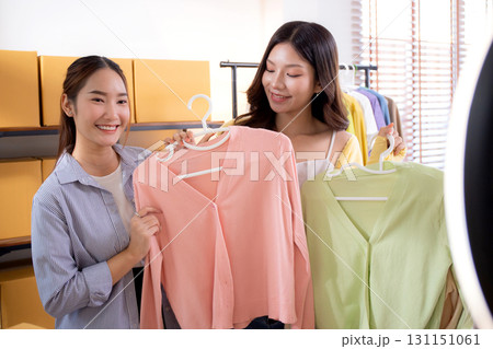 Two young asian woman live streaming online clothing store while showing clothing with smartphone. Two young asian woman live streaming online clothing store while showing clothing with smartphone. 131151061