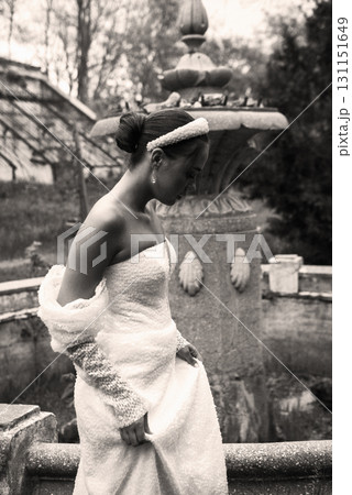A beautiful girl in a long white dress stands on white marble steps against the sky. 131151649