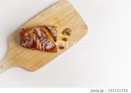 A delicious, warm, brown loaf of bread sits on a cutting board against a white background, decorated with autumnal objects. Studio photo. Concept photo. Top view. A delicious, warm, brown loaf of bread sits on a cutting board against a white background, decorated with autumnal objects. Studio photo. Concept photo. Top view. 131151728