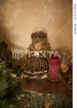Cute vintage doll sits on a shelf near a Christmas tree 131151948