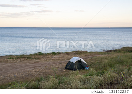 dark colored tent on grassy cliff on seashore. 131152227