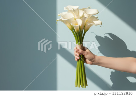 A hand holds a beautiful, elegant bouquet of fresh flowers against a bright, light blue background 131152910