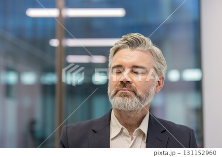 Businessman with closed eyes meditating, finding relaxation and balance, improving mental health and practicing mindfulness in a modern office environment Businessman with closed eyes meditating, finding relaxation and balance, improving mental health and practicing mindfulness in a modern office environment 131152960