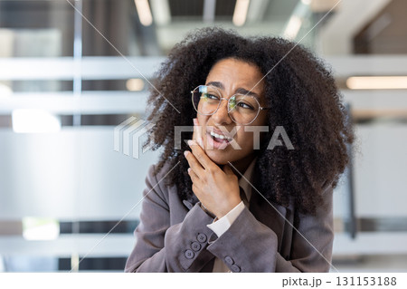 Close-up photo of a young African American woman in an office, sitting at a desk, suffering from a toothache. Close-up photo of a young African American woman in an office, sitting at a desk, suffering from a toothache. 131153188