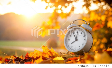 Clock against a vibrant autumn landscape showing golden leaves and warm sunlight 131153317