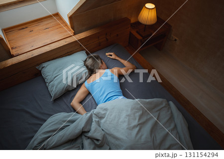 A person is peacefully sleeping in a cozy bedroom, surrounded by warm lighting and comfortable, inviting bedding A person is peacefully sleeping in a cozy bedroom, surrounded by warm lighting and comfortable, inviting bedding 131154294