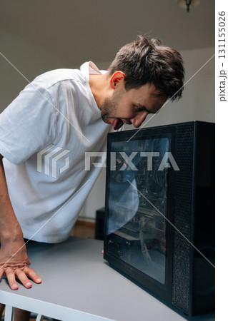 Vertical shot of computer technician male licking a dusty computer case with funny and frustrated expression, highlighting challenges of computer maintenance and repair. Concept of desktop PC service. Vertical shot of computer technician male licking a dusty computer case with funny and frustrated expression, highlighting challenges of computer maintenance and repair. Concept of desktop PC service. 131155026