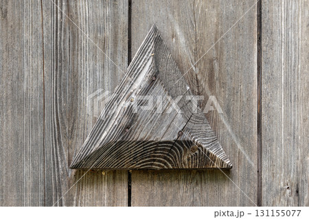 A weathered wooden triangle sits against gray planks, vintage door decor 131155077