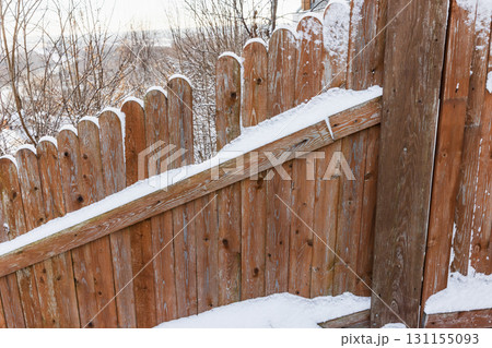 A wooden fence lines a snowy hillside, its diagonal beam capped with fresh snow 131155093