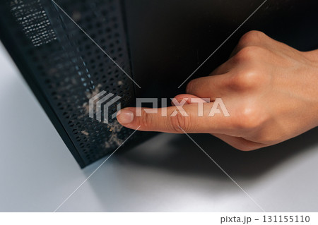 Close-up of technician pointing at thick layer of dust on computer air vents, emphasizing importance of regular cleaning and maintenance to avoid overheating and hardware failure. 131155110