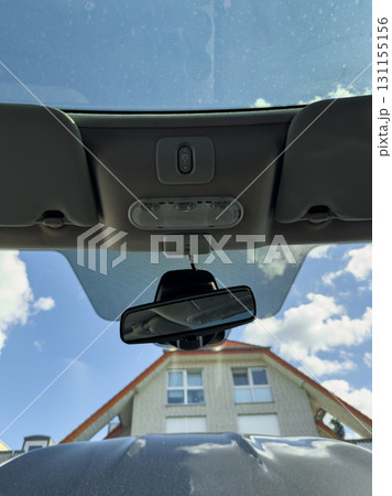 Clear sky seen through a car roof, mirror reflects a building in a suburban area during daylight hours 131155156