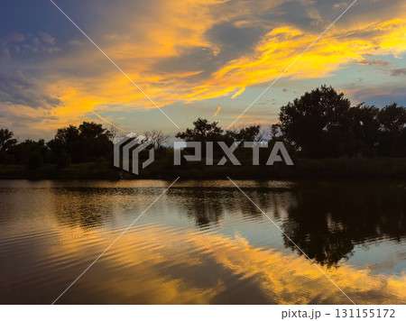 Vibrant sunset paints the sky and water with warm hues over a serene river landscape at dusk near quiet wooded banks 131155172