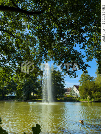 Tranquil park scene with a fountain surrounded by lush greenery and serene waters on a sunny day Tranquil park scene with a fountain surrounded by lush greenery and serene waters on a sunny day 131155463